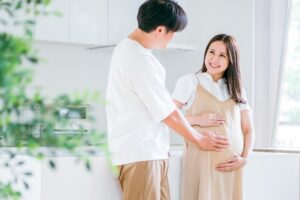 明るい部屋で、カップルが仲良く未来を語るように微笑んでいる。女性はお腹を優しくさすっている画像